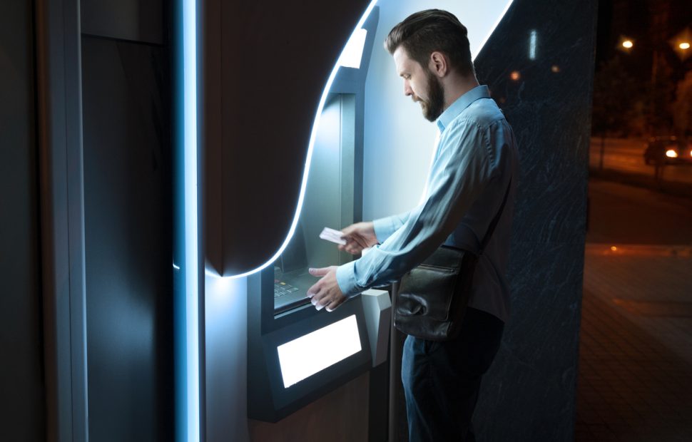 Business professional withdrawing cash from a modern ATM at night demonstrating real-world ATM usage in 2026